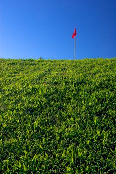 Grass hill with red flag and deep blue sky