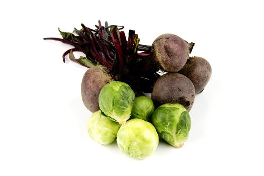 Bunch of raw red beetroot with a pile of small green sprouts on a reflective white background