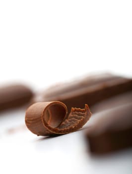 Close-up facture of a curl of chocolate on white with a piece of chocolate at the background