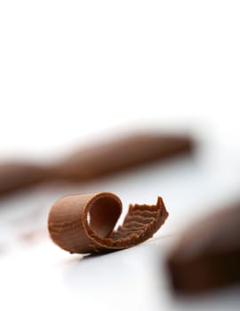 Close-up facture of a curl of chocolate on white with a piece of chocolate at the background