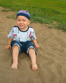 The barefoot little boy, sitting on sand.