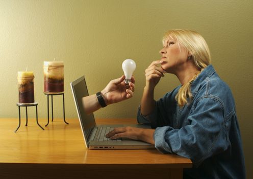 Attractive businesswoman deep in creative thought while a hand holding a light bulb comes out of her screen