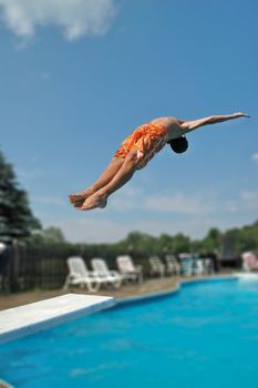A boy does a dive off of a diving board at a home swimming pool of blue water.