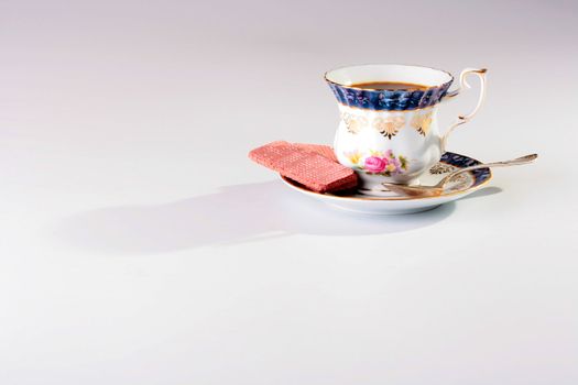 Cup of black coffee on a saucer with a spoon and wafers in ceramic ware.