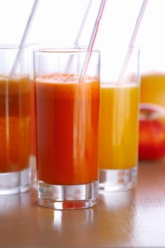 Three glasses of different juice on the table with straw in the and fruits behind them .