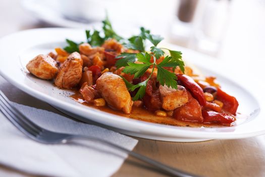 Focus on the plate of goulash with green parsley on it and fork on napkin beside it.