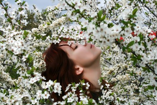 A beautiful girl enjoying the sunny weather in the middle of blooming cherry tree