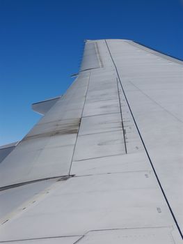 Wing of a jumbo jet taken POV from inside the aeroplane looking out into a pure blue sky
