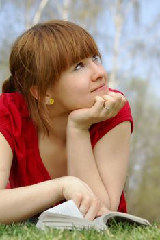 Young girl lying with a book on spring grass in a park and dreaming 