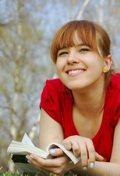 Young girl lying with a book on spring grass in a park and dreaming 