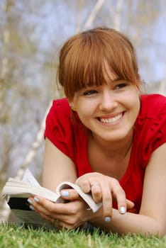 Young girl lying with a book on spring grass in a park and laughing