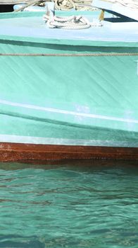 Turquoise boat hull in water with the reflection of the water playing on the side of the boat