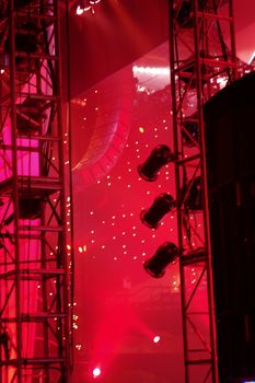Backstage view of the stage with lighting and scaffolding mainly in silhouette against  bright red 
