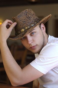 Young, handsome, seated, cowboy tipping his hat towards the camera