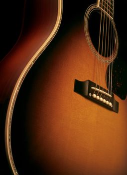 Angle shot of a maple wood acoustic guitar showing wood grain, bridge and strings.
