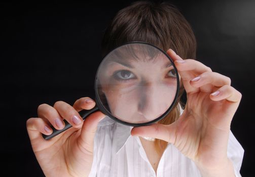 Young woman holding magnifying glass on black background