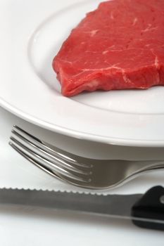 Dinner plate with raw red meat and cutlery.
