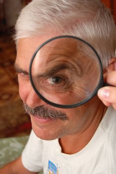 Mature man and magnifier on his eye