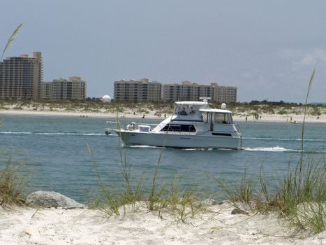A white yacht is slowly cruising by and against the background of a vacation resort and the beach in Ponce Inlet.