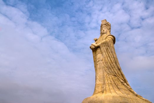 Chinese god statue of Mazu in golden color with blue cloud sky background.