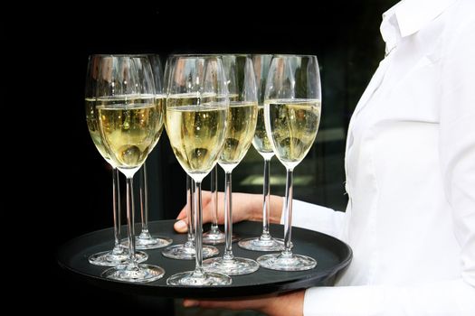 A waiter with champagne glasses on a tray. The background is black