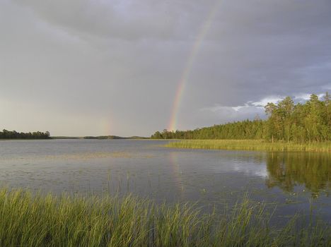 The rainbow in the cloudy sky is reflected in wood lake 