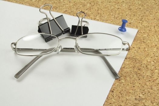 chrome spectacles and bulldog clips on a piece of paper pinned to a notice-board