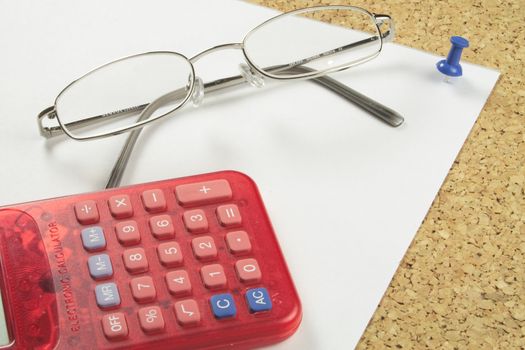 spectacles with a calculator on a piece of notepaper pinned to a board
