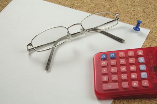 spectacles with a calculator on a piece of notepaper pinned to a board
