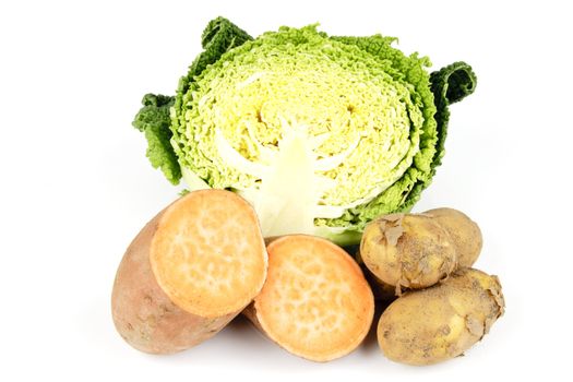 Half a raw green cabbage with a single sweet potato cut in half and a pile of brown potatoes on a reflective white background