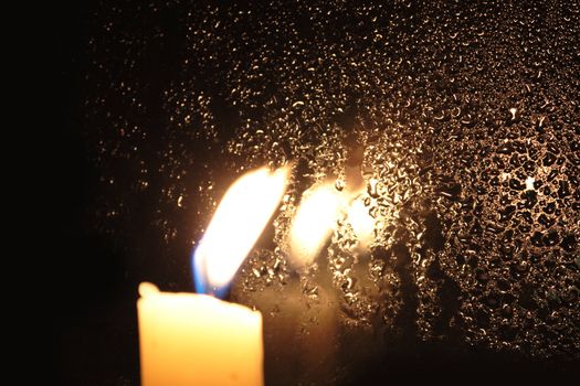 Candle with burning flame on background with dark wet window