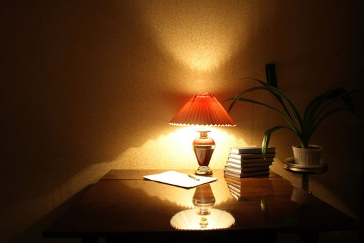 Evening home interior with luminous lamp and stack of books on the table