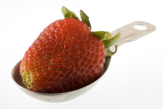 a single strawberry fruit on a measuring tablespoon, white background