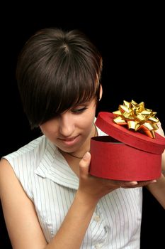 The young girl looks in a box with a gift, isolated on black background