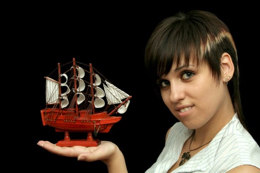 The nice smiling girl with the toy ship in a hand, isolated on black background