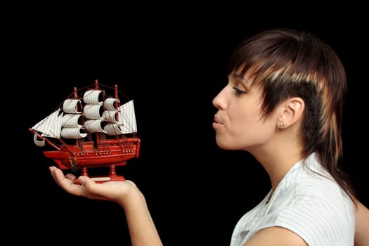 The nice girl blows on a toy ship in a hand, isolated on black background