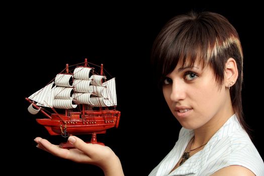 The nice smiling girl with the toy ship in a hand, isolated on black background