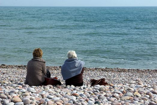 Senior ladies sitting on a pebble beach in Devon, with a view on the sea