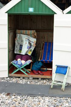 Photo of a person reading a newspaper in a beach cabin