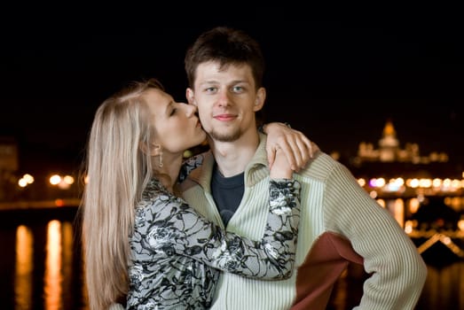 A young man and a young woman kissing on the night bridge