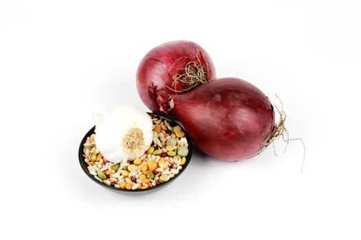Two raw unpeeled red onions with soup pulses in a small black dish and garlic on a reflective white backgrounds