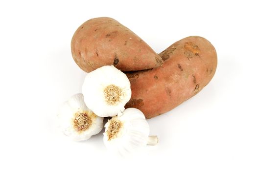 Two raw unpeeled sweet potatoes with white garlic bulbs on a reflective white background