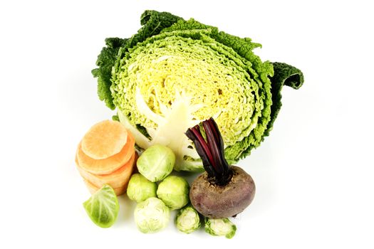Half a raw green cabbage with raw beetroot, sprouts and slices of sweet potato on a reflective white background