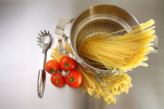 Overhead shot of pasta, tomatoes and pot on stainless steel counter