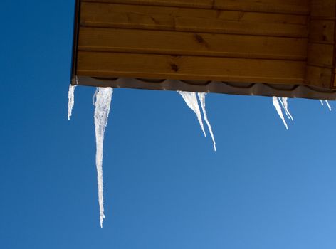 Icicles on a wooden roof against the blue sky.