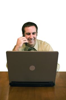 A happy man working from home with his cell phone and laptop.  Shallow depth of field with focus on the laptop computer.  Includes clipping path.