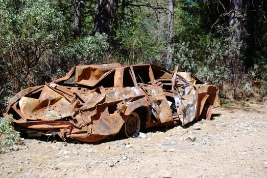 An abandoned old car with bullet holes, crushed and rusty  from being burnt parked in the forest.