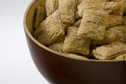 a wooden, round, bowl of shredded wheat cereal (dry, no milk), white copy space