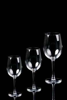 Three empty glasses over black background with reflection. Water, white wine and red wine.