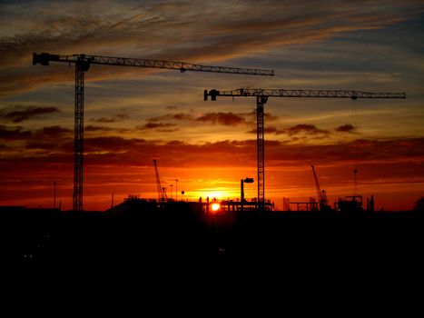 Cranes and construction site silhouette against setting (or rising) sun